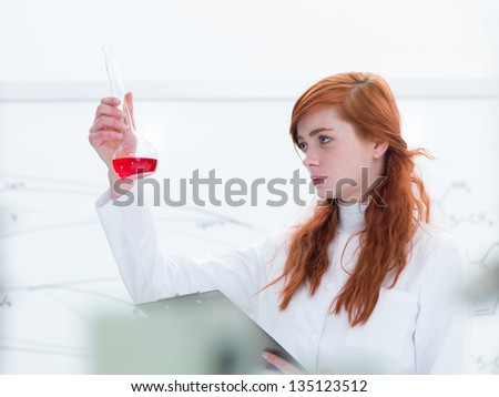 close-up of a beautiful girl student in a chemistry lab analyzing colorful substances and a white board on the background