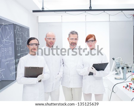 general-view of smiling researchers team in a chemistry lab around lab table with lab tools and colorful liquids