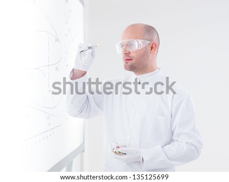 side-view  of a scientist in a chemistry lab holding in his hands and analyzing a white-yellow pill in front of a whiteboard