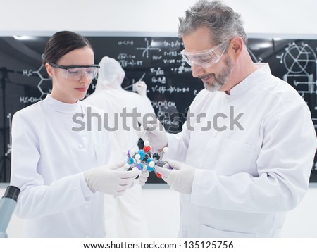 general-view of a teacher and a student in a chemistry lab analyzing molecular structure of dmt with another student on the background writing formulas on a blackboard