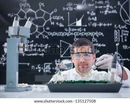 close-up of a man in a chemistry lab conducting a plant experiment on a lab table with lab tools and a blackboard on tha background