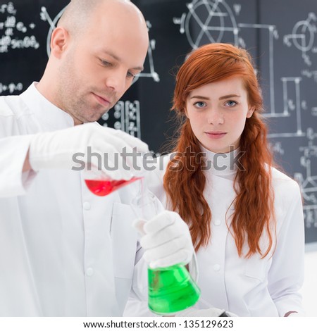 close-up of student looking in the camera and a teacher conducting a lab experiment with colorful liquids  and lab tools and a blackboard on the background