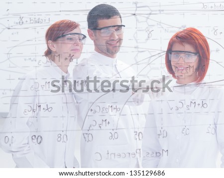 close-up seen through a transparent board of one teacher in a chemistry lab  pointing formulas for his student on  a transparent  board and one student smiling in the camera