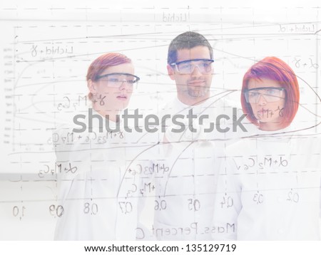 close-up seen through a transparent board ot three scientists in a chemistry lab  pointing and analyzing formulas on it