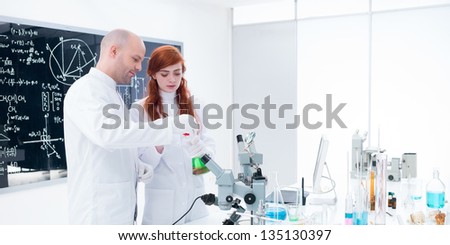 side-view  of a teacher conducting a lab experiment with a student  around the lab table with lab tools, colorful liquids and a blackboard on the background