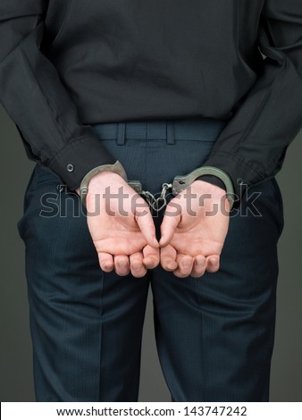 back view of a person dressed in black; hancuffed with their hands behind their back and their palms open