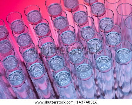 top view, macro of test tubes, some empty and some filled with transparent floating substance above transparent colorless liquid, against a gradient pink and purple background