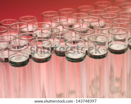 Gradient red background and a macro of a group of pellucid test tubes with dark solution at the surface and colourless inwards