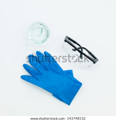 aerial view of a pair of blue lab gloves, protective goggles and an empty bottle on a white table