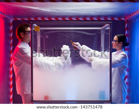 two scientists, a man and a woman, mixing chemicals in a sterile chamber labeled as bio hazardous filled with white steam, the woman holding a brown bottle, in a containment tent