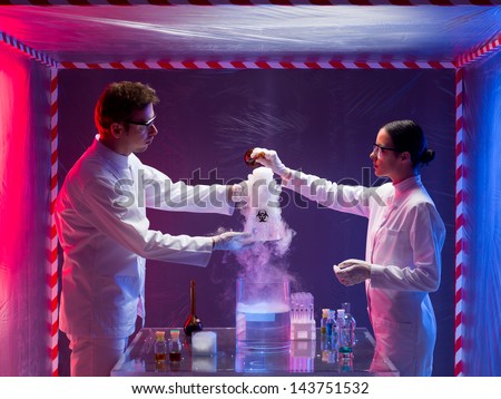 two scientists, a man and a woman, mixing chemicals in a containment tent, holding a glass container labeled as bio hazardous filled with white pouring steam