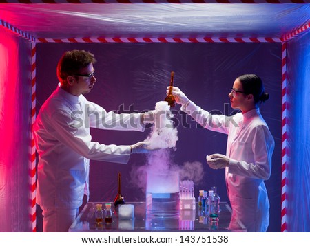 Photograph of a male and female scientists inside a biohazard protective space testing the toxic chemicals while the smoke coming out.