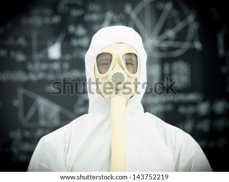 person in protective gear with gas mask in front of a blackboard  with graphics and formulas written on it in chalk