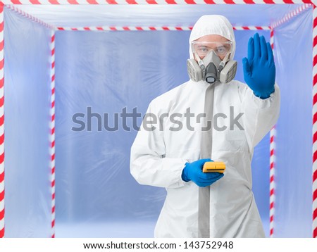 Person in biohazard suit calling a halt by raising a hand in the air while standing in front of a containment tent holding a digital counter or tester