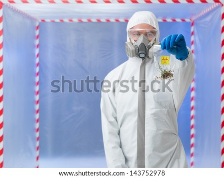 close-up of man wearind protection equipment, holding a plastic bag with germinated seeds, in a chamber surounded with red and white tape