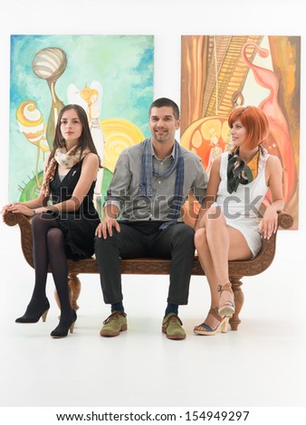 front view of three young caucasian people sitting on a bench in a museum, with colorful artwoks in background