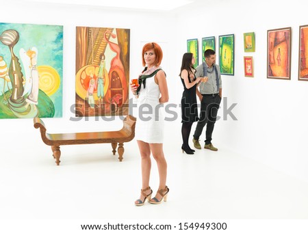 beautiful caucasian woman standing in an art gallery with other people contemplating art in background