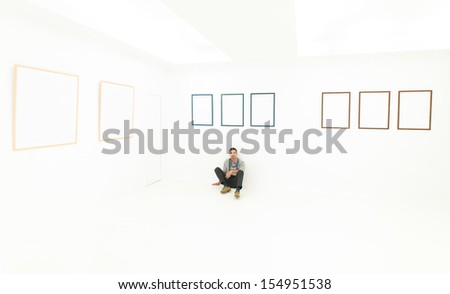 man sitting on the floor in a relaxed position, in a white room with empty frames displayed on walls