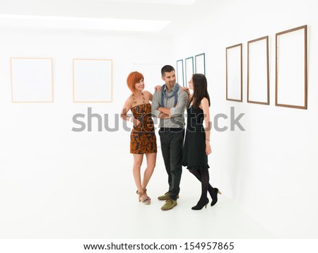 young beautiful women holding her hands on a man\'s shoulders and smiling in a room with empty frames displayed on white walls