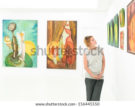 Beautiful Caucasian Woman In Art Gallery Leaning Against A Wall With Colorful Paintings