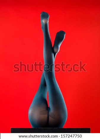 woman wearing pantyhose lying on her back with her feet up on red background