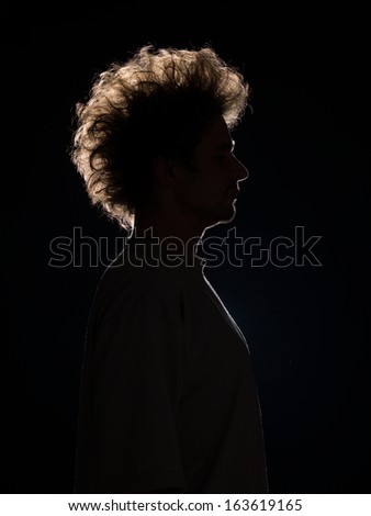 profile of man in black shadow with tousled hair on black background