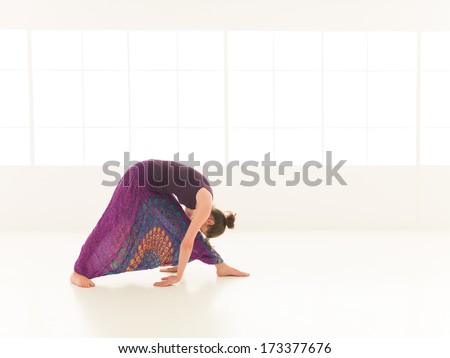 side view of young woman in yoga posture, face obscuredm dressed colorful, iluminated window backgrond