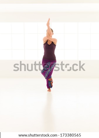 young woman sitting in difficutl yoga pose, full frontal view, face obscured, dressed colorful, iluminated window background