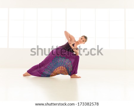 young  girl in twisted yoga posture, dressed with pants skirt colorful indor