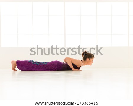 young woman in balancing yoga pose, side view, full body, dressed colorful, iluminated window backgrond