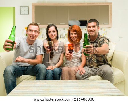 friends sitting at home on sofa, making a toast with drinks and watching tv