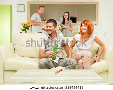 friends at home having party, some of them sitting on couch while other ones dance in background