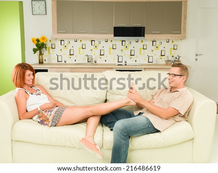 young caucasian happy couple relaxing on sofa, man giving foot masssage to his girlfriend