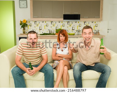 two men sitting on couch watching television, in kitchen, holding beers and screaming, with an upset woman between them