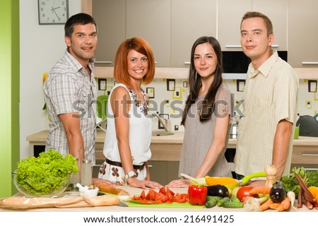 front view of young caucasian friends standing in the kitchen and smiling, with vegetables on table