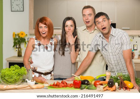 portrait of four young caucasian people standing in kitchen, table with colorful mixed vegetables, acting surprised