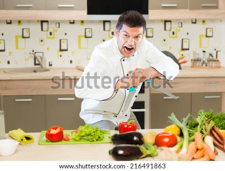 angry chef standing in front of table with vegetables, holding two knifes