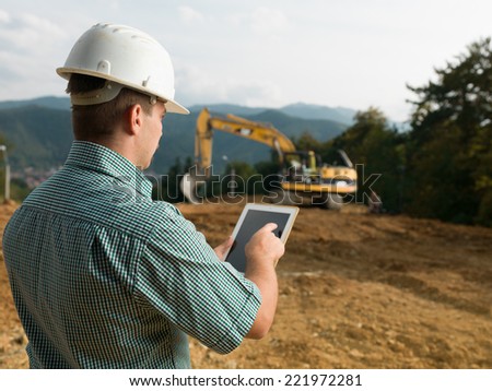 back view of caucasian engineer standing on construction site checking plan on digital tablet