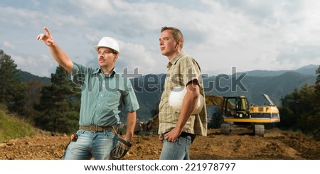 two caucasian engineers standing, one of them pointingat construction in progress