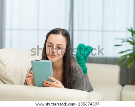 beautiful young caucasian girl lying on sofa and playing games on digital tablet