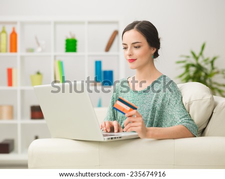 portrait of young caucasian woman looking at laptop, holding credit card and spending money online while relaxing at home
