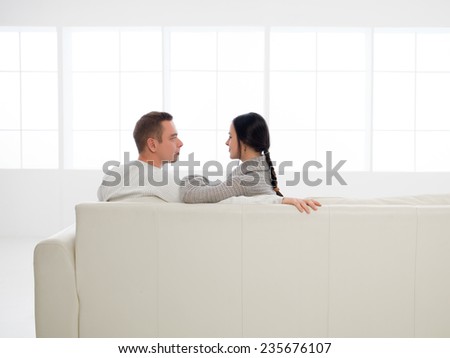 back view of young happy caucasian couple sitting on sofa in new house