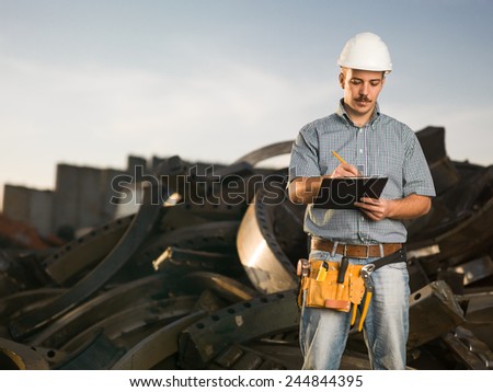 portrait of caucasian worker standing in metal landfill outdoors, writing
