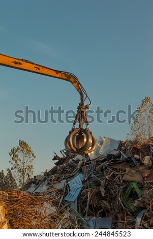 crane holding scrap metal on top of pile of junk