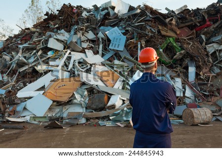 worker standing in front of pile of disposed objects in recycling center
