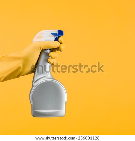 hand with rubber glove holding cleaning spray container on yellow background