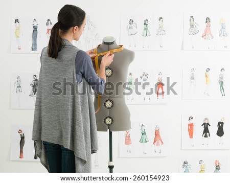 young caucasian female fashion designer taking measurements on mannequin in her studio