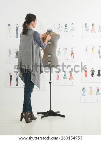 young caucasian female fashion designer taking measurements on mannequin in her studio
