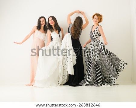 beautiful caucasian women in cocktail dresses posing together, dancing and having fun, against white background