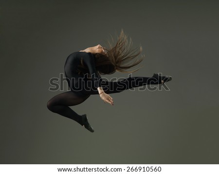 dancer performing high jump against grey background